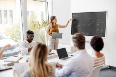 Presentation in Multi-Ethnic Office Conference Room. Meeting of Diverse Young Entrepreneurs, Specialists, Talking, Using TV for infographics. Businesspeople Develop e-Commerce Startup